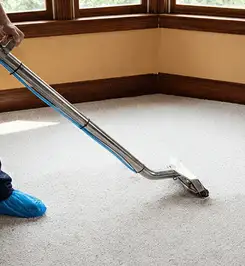 Steam carpet cleaning technician using a hot-water extraction wand on a residential carpet, wearing blue protective shoe covers Duluth, MN.