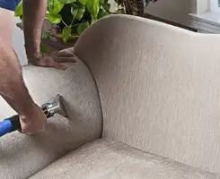 Professional upholstery cleaner deep-cleaning a fabric sofa with a handheld extraction tool and hose in Duluth, MN.